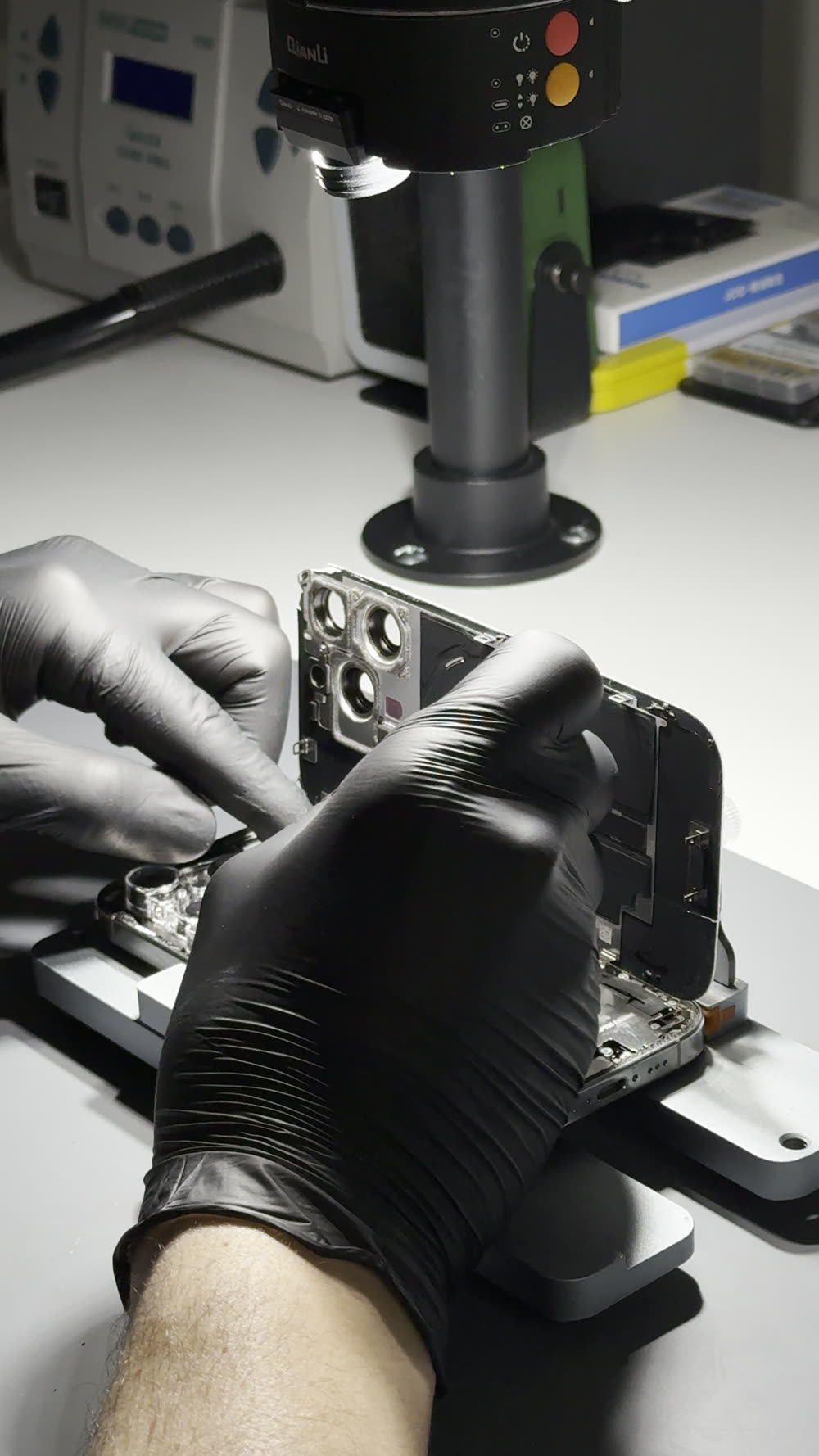 Cuadro del video de Feex: dos manos con guantes negros abriendo un iPhone bajo el microscopio del taller